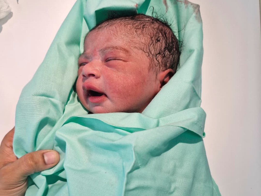 A newborn baby swaddled in a green cloth shortly after delivery
